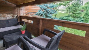 A covered patio with wicker furniture and a view of a garden.