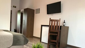 Ein Schlafzimmer mit Bett, Schreibtisch, Stuhl, kleinem Kühlschrank und Topfpflanze.