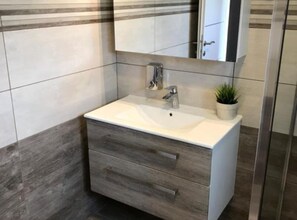 Bagno con lavandino bianco, uno specchio e una pianta in vaso.
