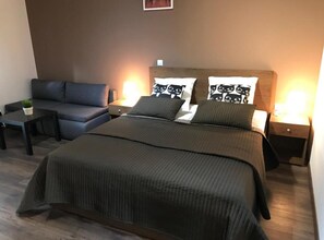 Un dormitorio ordenado con una cama grande, un sofá, dos mesitas de noche y una pequeña mesa con una planta.