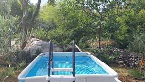 Piscina elevada con escalera, rodeada por un paisaje natural con árboles y rocas.