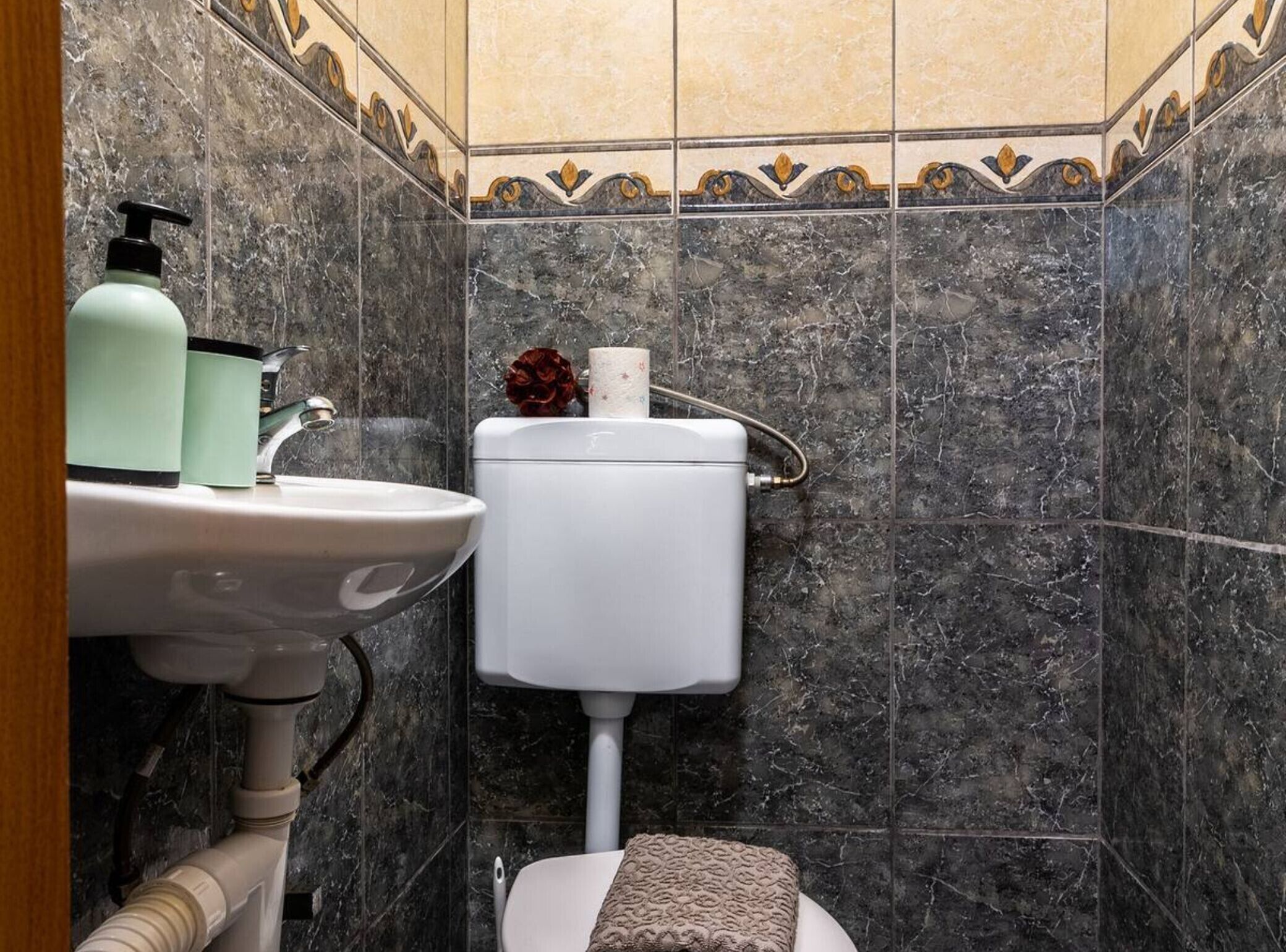 A bathroom with a white sink, a toilet, and a marble-tiled wall.