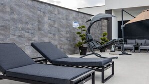 Terraza en la azotea con sillones de descanso, una hamaca colgante y una planta en maceta.