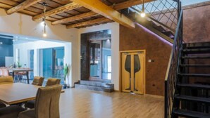 Una habitación amplia con techo de madera, un comedor con mesa y sillas, y una escalera con barandilla de metal.