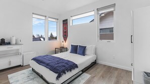A modern bedroom with a bed, a nightstand, a dresser, and a window with a view. - Highgarden The Tyrell House Sweet Suite (Seattle)