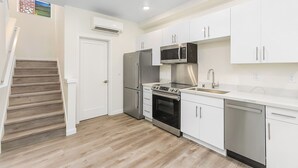 A modern kitchen with white cabinets, stainless steel appliances, and a wooden staircase. - Highgarden The Tyrell House Sweet Suite (Seattle)