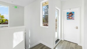 A hallway with white walls, a door with a painting, and an exit sign. - Highgarden The Tyrell House Sweet Suite (Seattle)