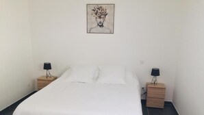 Una cama bien hecha con ropa blanca, dos mesitas de noche con lámparas y una obra de arte colgada en la pared.