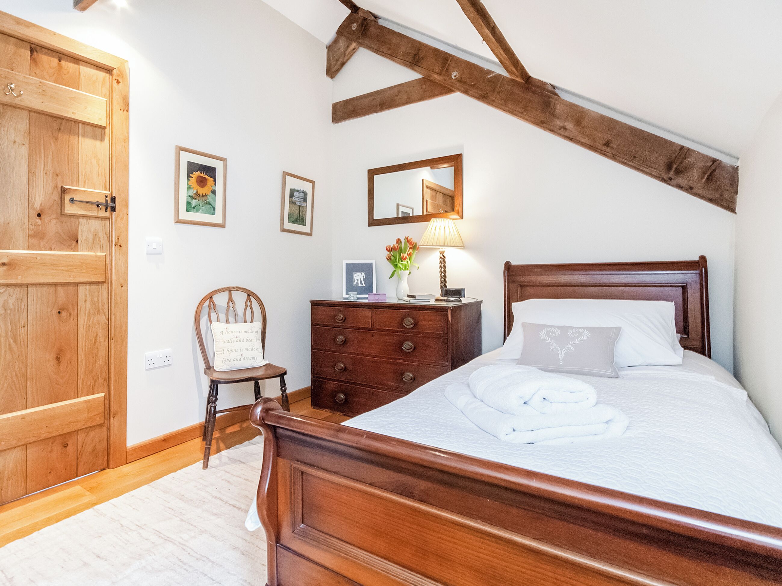 Un dormitorio con una cama y cómoda de madera, una silla y una puerta de madera.