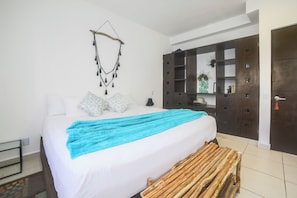 A bedroom with a bed, a blue blanket, a wooden bench, a wardrobe, and a wall-mounted decoration.