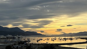 A marina with boats docked, a bridge, and mountains in the background.