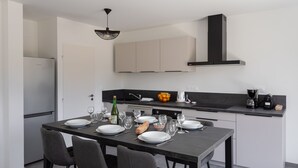 Une cuisine moderne avec une table à manger pour quatre personnes, équipée d’un réfrigérateur, d’un four et d’une hotte aspirante noire.