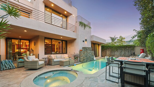 Una casa moderna con piscina, mobiliario de exterior y un muro de piedra.