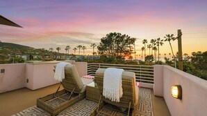 Una terraza en la azotea con sillones de mimbre, un tapete estampado y vistas al atardecer.