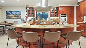 Una cocina moderna con una isla central, taburetes de bar, armarios de madera y un ventanal grande.