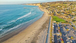 Un paisaje urbano costero con una playa, un muelle y un estacionamiento.