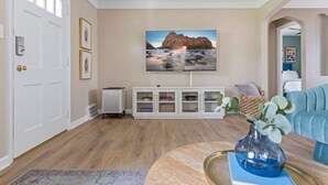 Un salon avec un grand téléviseur à écran plat fixé au mur, un meuble de rangement blanc en dessous, et un canapé bleu placé au premier plan.