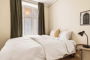Relax in a spacious room with a large bed, a small table, and a lamp.