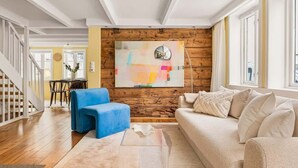 Ein Wohnzimmer mit einer Holzwand, einem blauen Sessel, einem beigen Sofa und einem modernen abstrakten Gemälde.