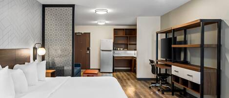 A hotel room with a large bed, a desk, a TV, and a kitchenette.