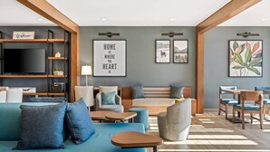 A modern living room with a sofa, armchairs, a coffee table, and a TV. There are framed pictures on the wall and a sign that says "HOME IS WHERE THE HEART IS". - Everhome Suites Bozeman (Bozeman)