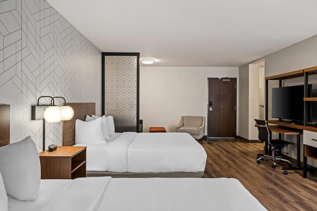 A hotel room with two beds, a desk with a computer, a TV, and a chair.