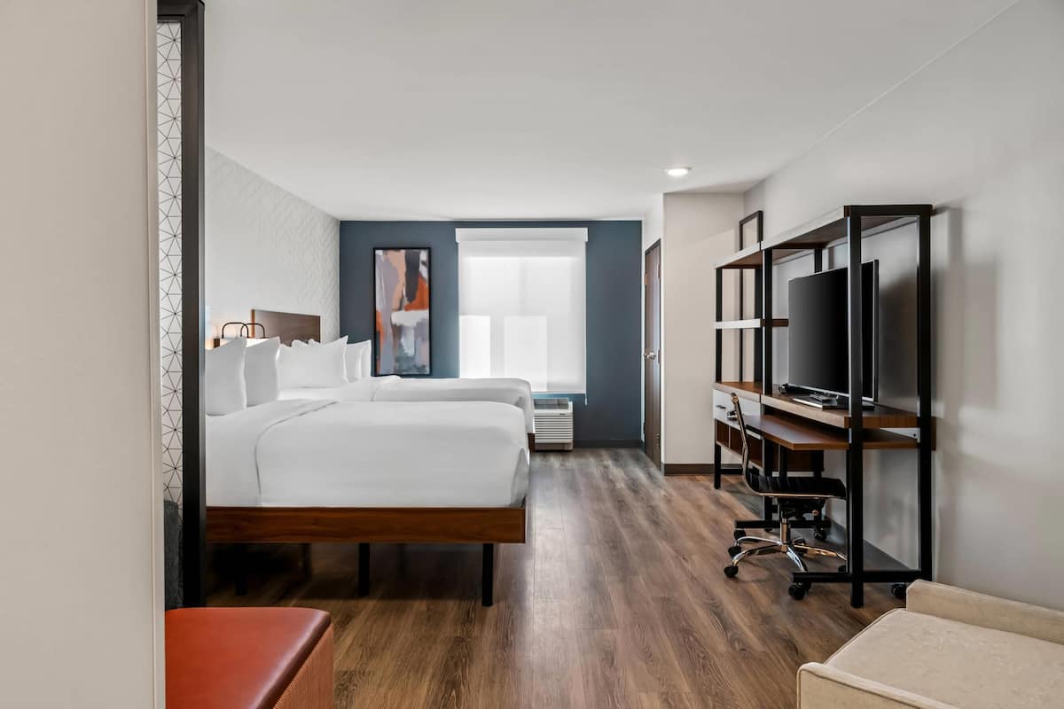 A hotel room with a large bed, a desk with a computer, a television, and a window with blinds.