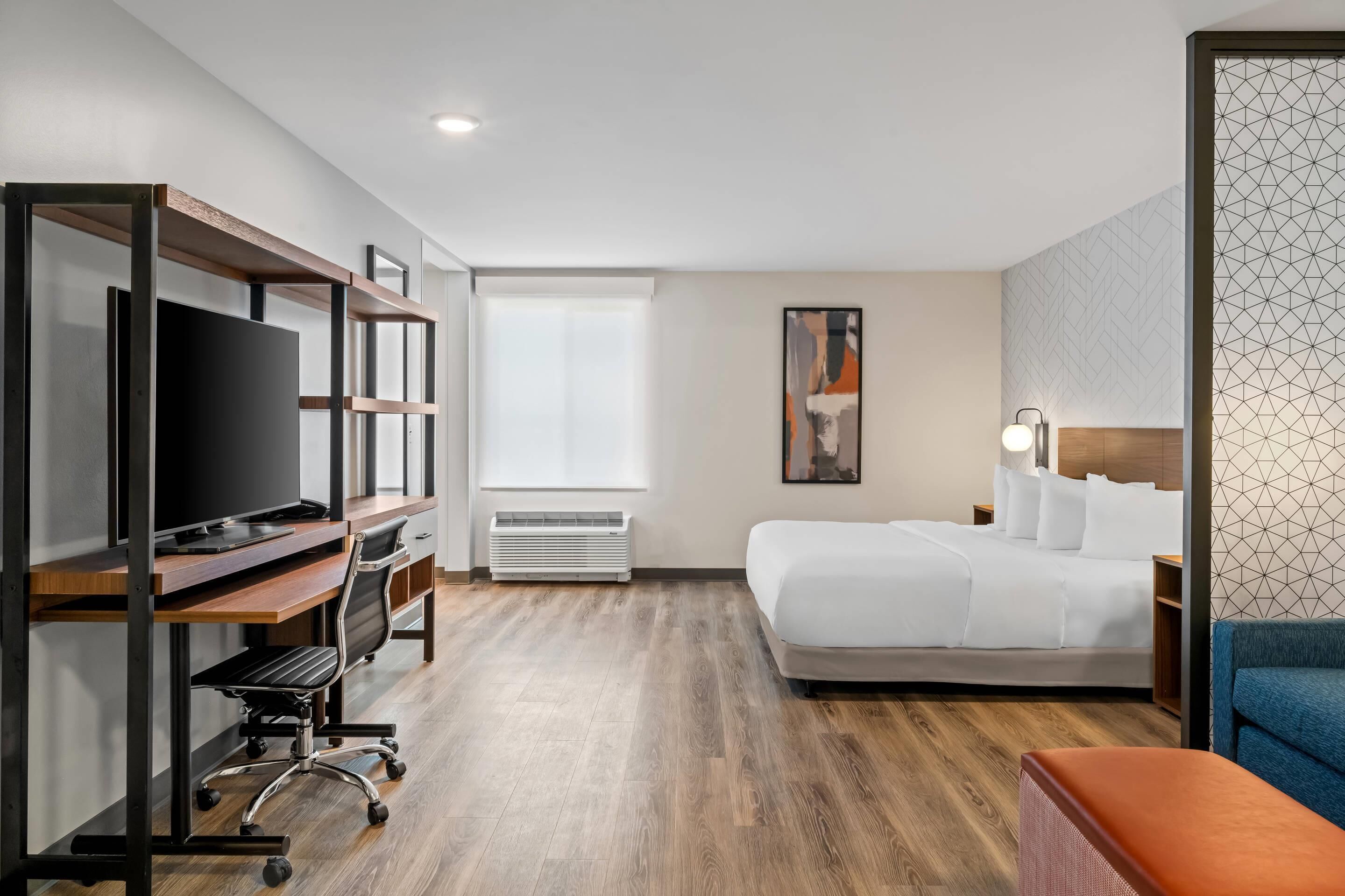 A hotel room with a bed, a desk with a computer, a TV, and a seating area.