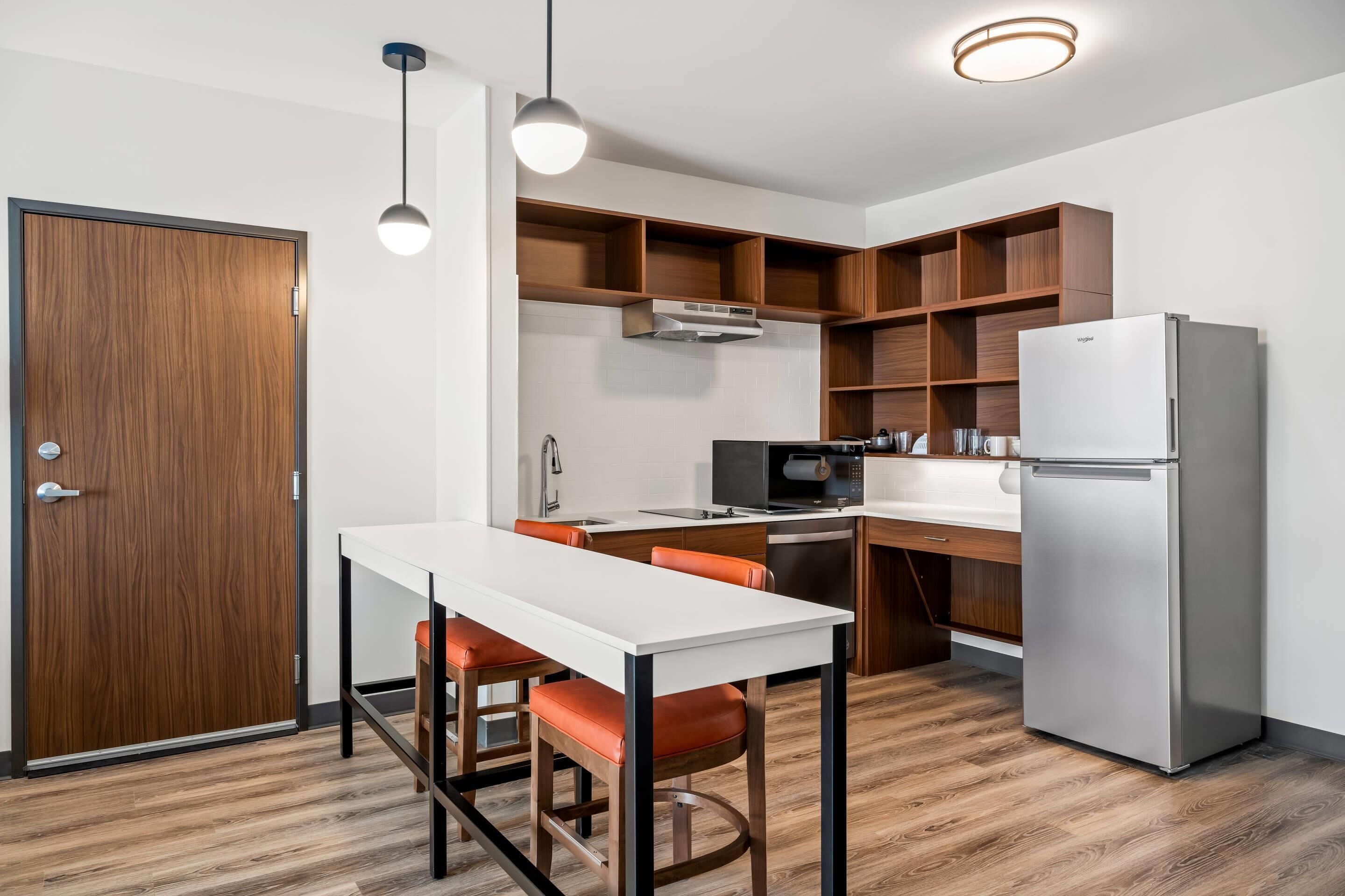 A modern kitchen with a white countertop, stainless steel appliances, and wooden shelving.