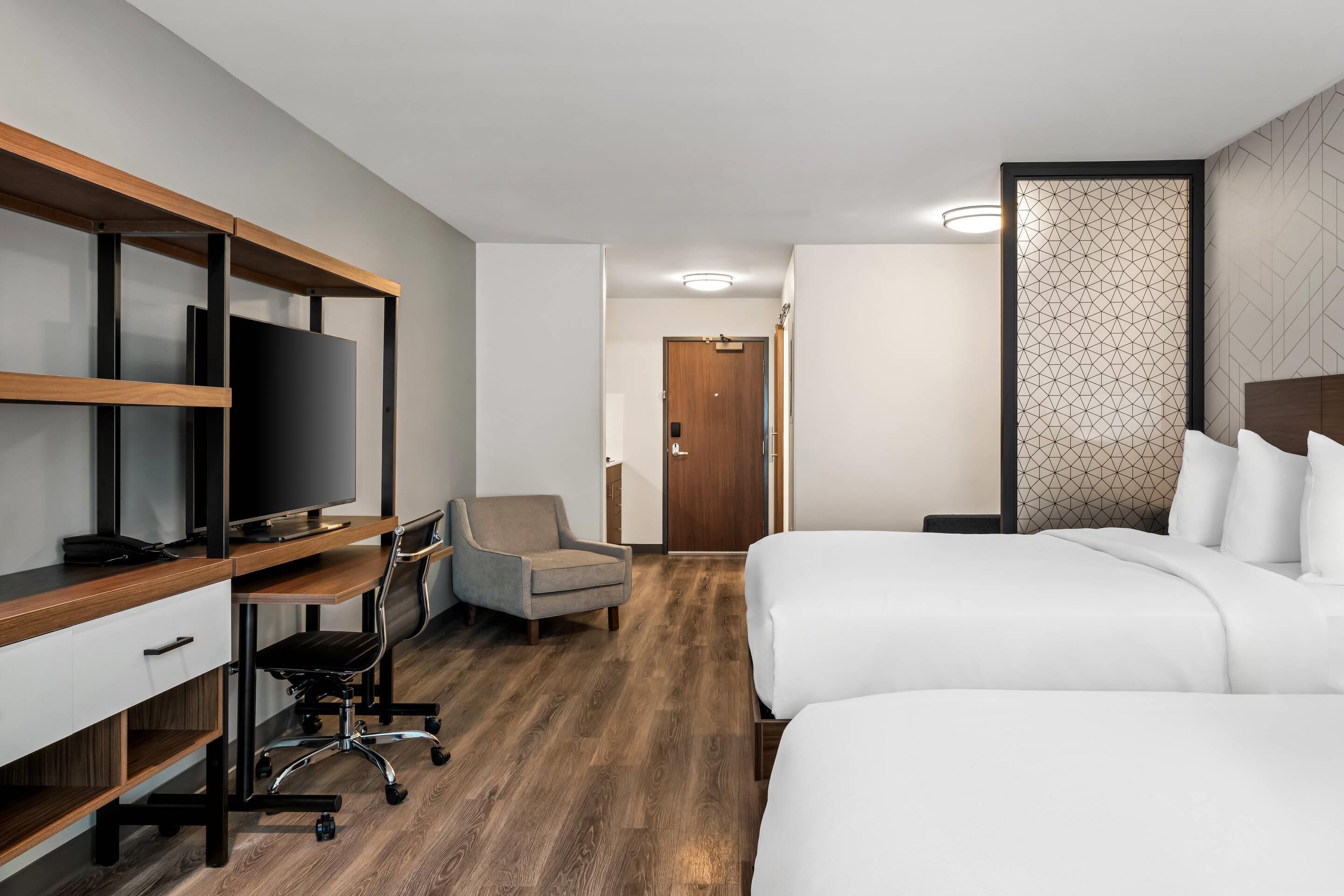 A hotel room with a wooden desk, a television, a chair, and a bed.