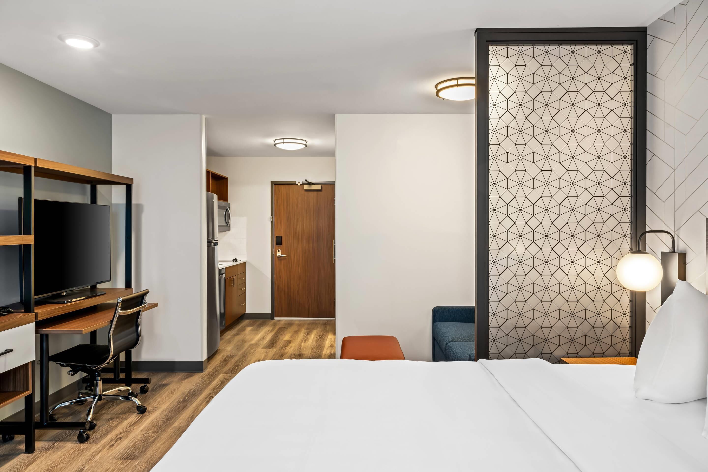 A hotel room with a bed, a desk with a chair, a television, and a wardrobe.