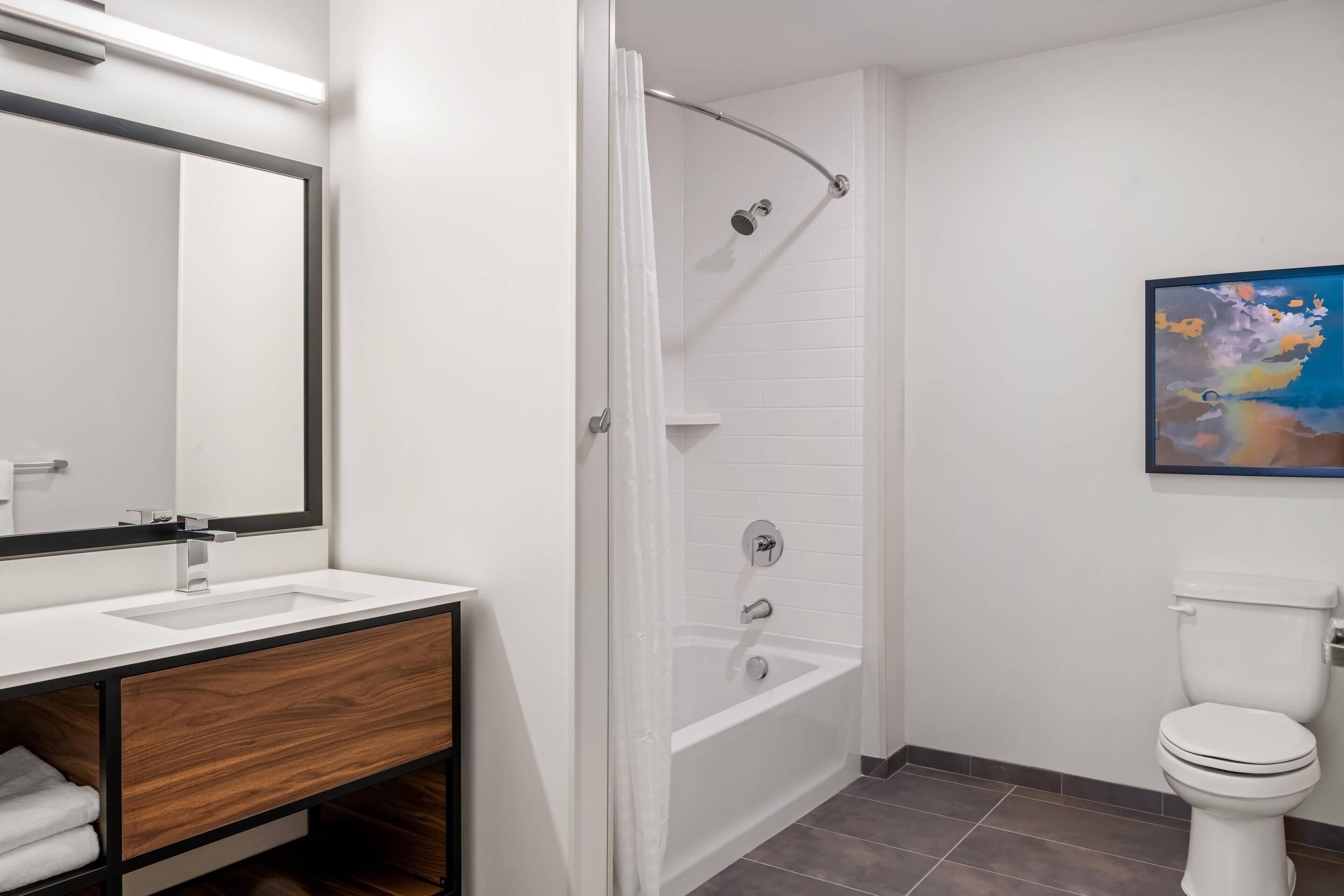 Un baño moderno con lavamanos blanco, tocador de madera, bañera y retrete.