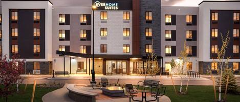 Un hotel moderno con varios pisos, mobiliario exterior y una entrada bien iluminada.