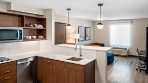A modern kitchen with a built-in microwave, a dishwasher, and a sink. There is a dining area with a table and chairs, and a window providing natural light. - Everhome Suites Bozeman (Bozeman)