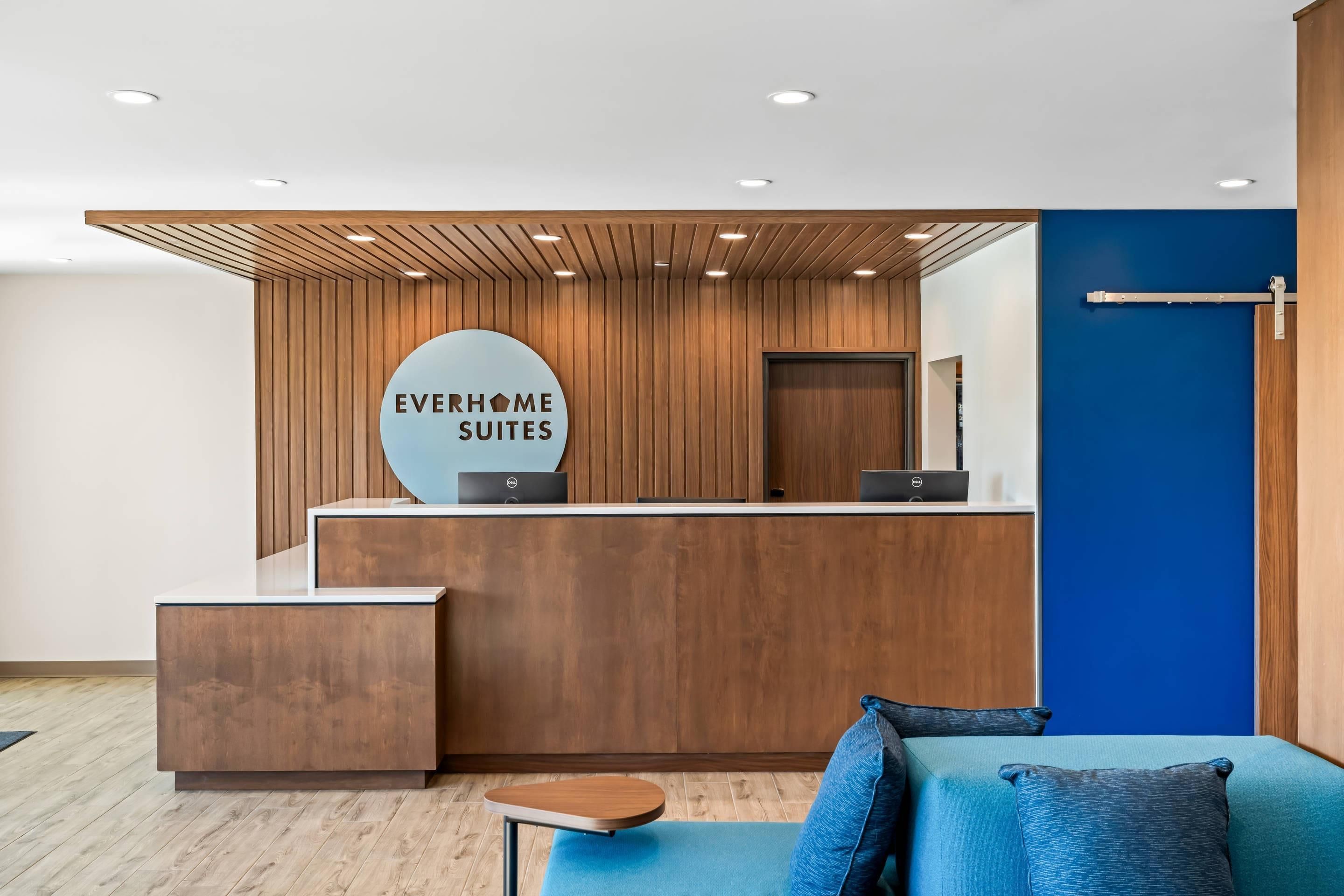 A reception desk with a sign reading 'EVERHOME SUITES' and a blue wall with a door.