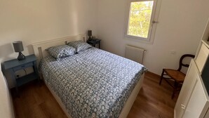 Un dormitorio con cama, mesita de noche, silla, ventana y radiador.