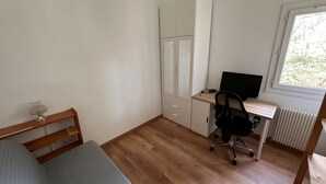 Un dormitorio con cama, escritorio, silla y ventana.
