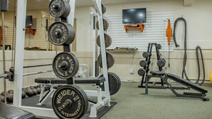 Une salle de sport équipée de matériel de musculation, d’un banc et d’un téléviseur fixé au mur.