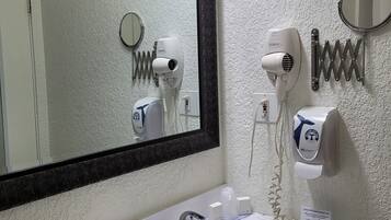 Un baño con lavamanos, espejo, secador de pelo y toallero.