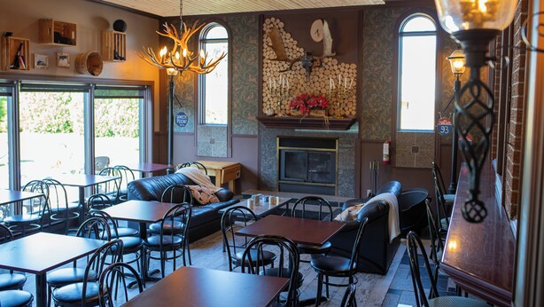 L’intérieur de ce restaurant est chaleureux, avec une cheminée, un plafond en bois et différents types de sièges, notamment des tables et des canapés.