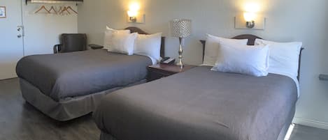 A hotel room with two beds, a chair, a nightstand with a lamp, and a coat rack with hangers.