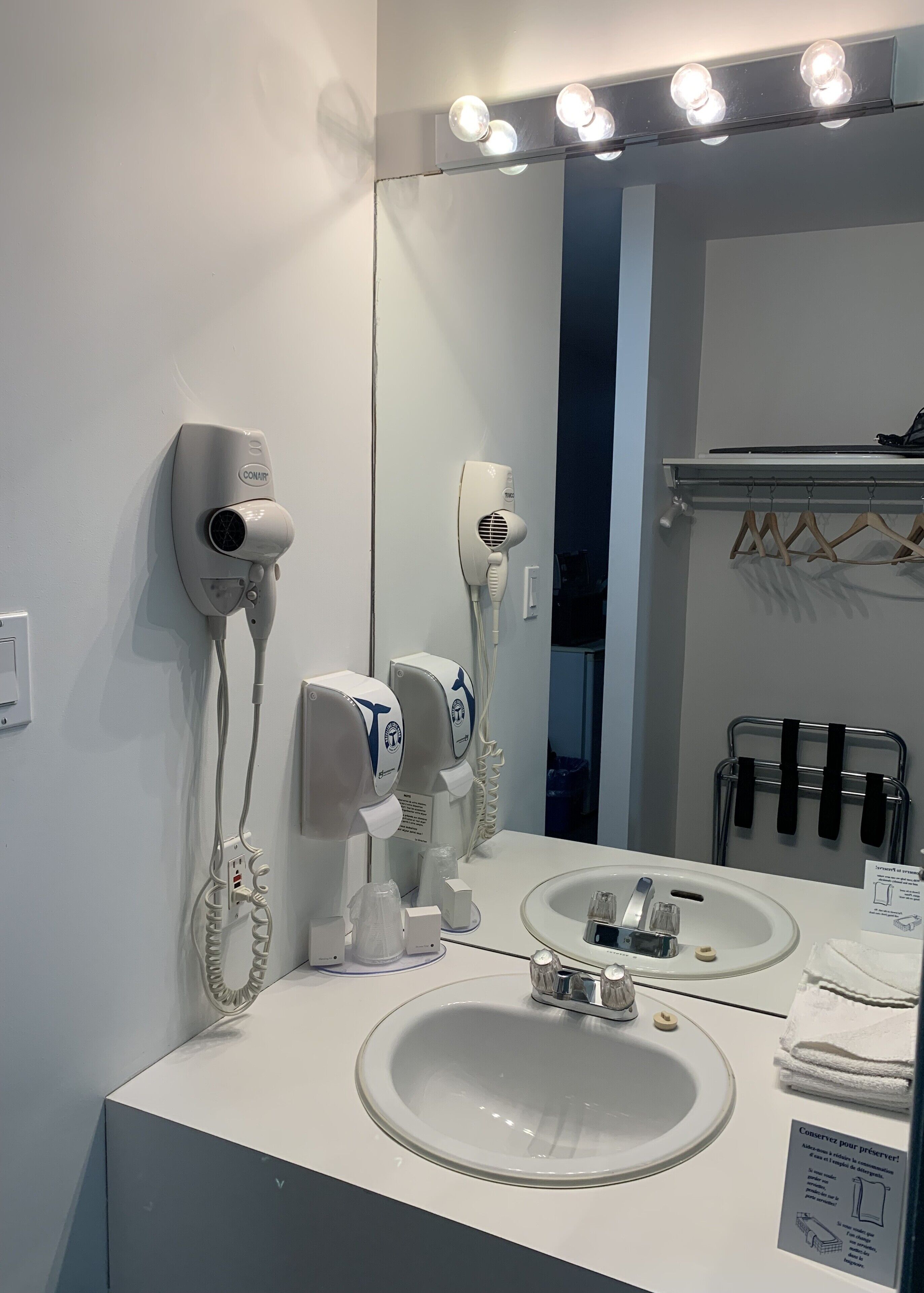 Een badkamer met een wastafel, twee haardrogers, een spiegel en een handdoekrek.