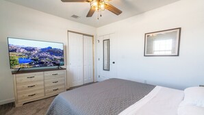 A bedroom with a bed, a television on a dresser, a ceiling fan, and a mirror.