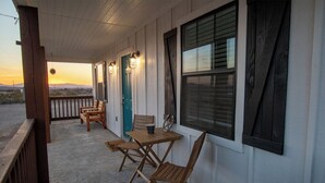 A covered porch with a wooden bench and table, a teal door, and a window with blinds.