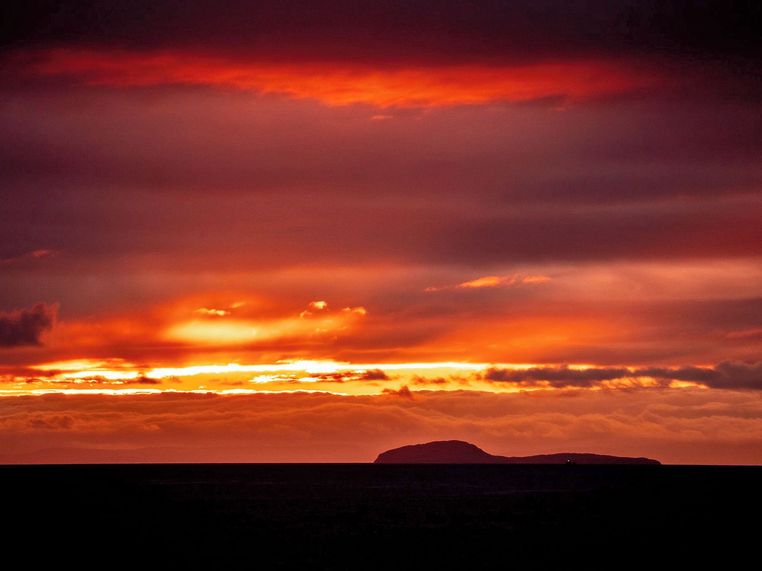 A sunset over a mountainous landscape with a silhouette of a mountain in the foreground.