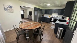 Une cuisine moderne avec des meubles de couleur sombre, des appareils en acier inoxydable et une table de salle à manger ronde en bois, assortie de chaises.