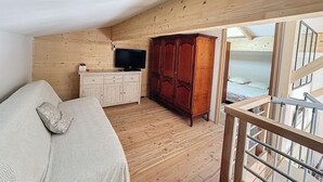 A wooden cabin room with a bed, a TV, a wardrobe, and a staircase leading to an upper level. - Chalet Familial Dans les Monts D'ardèche (La Souche)