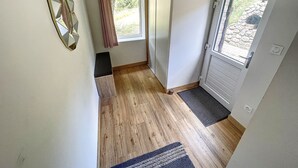 A narrow hallway with wooden flooring, a bench, a mirror, a window with curtains, and a door with a view of the outside. - Chalet Familial Dans les Monts D'ardèche (La Souche)