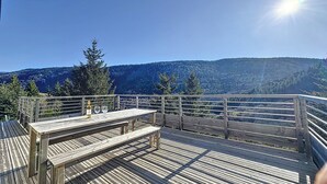 A wooden deck with a table and benches, overlooking a forested mountain range. - Chalet Familial Dans les Monts D'ardèche (La Souche)
