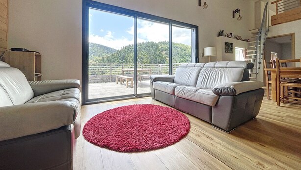 A spacious living room with a large sliding glass door leading to a deck with a scenic mountain view. - Chalet Familial Dans les Monts D'ardèche (La Souche)